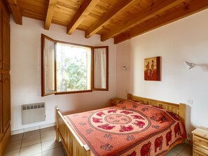 A bedroom with a wooden bed, a window with curtains, a radiator, and a painting on the wall.