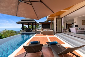 A luxurious outdoor pool area with a clear view of the ocean, a covered seating area, and a modern interior with a sofa and dining area. - Vista Mar (Koh Samui)
