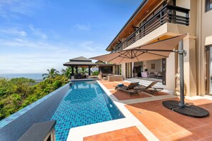 A modern pool area with a view of the ocean, outdoor seating, and a covered patio. - Vista Mar (Koh Samui)
