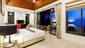 A modern bedroom with a large bed, a TV, and a balcony with a view of the night sky. - Vista Mar (Koh Samui)