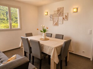 A dining area with a table set for six, six chairs, a vase with flowers, and wall art.