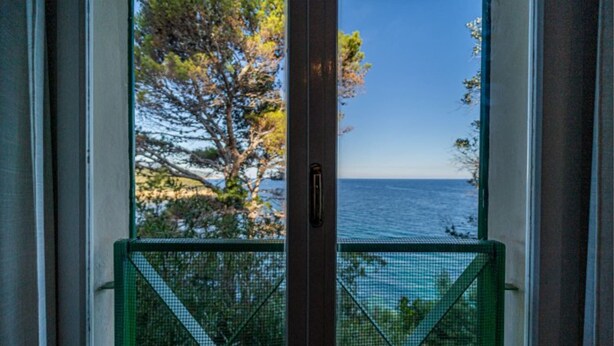 A view through a window with a metal gate, overlooking a body of water and trees. - Villa Tramonto facing the seashore (Portoferraio)