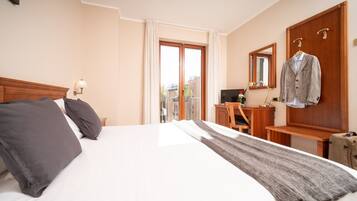A hotel room with a large bed, a desk, a chair, a mirror, and a coat rack.