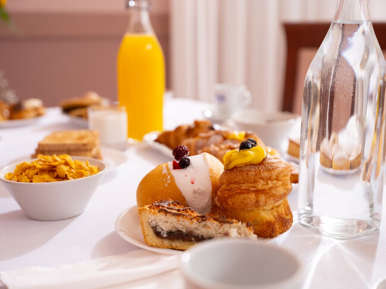 A breakfast table with pastries, a bottle of orange juice, and a glass of water.