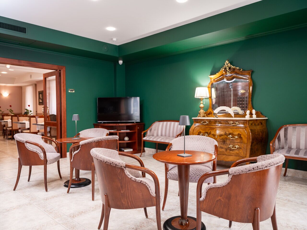 Habitación de hotel con paredes verdes, cómoda de madera, televisor y muebles de mimbre.