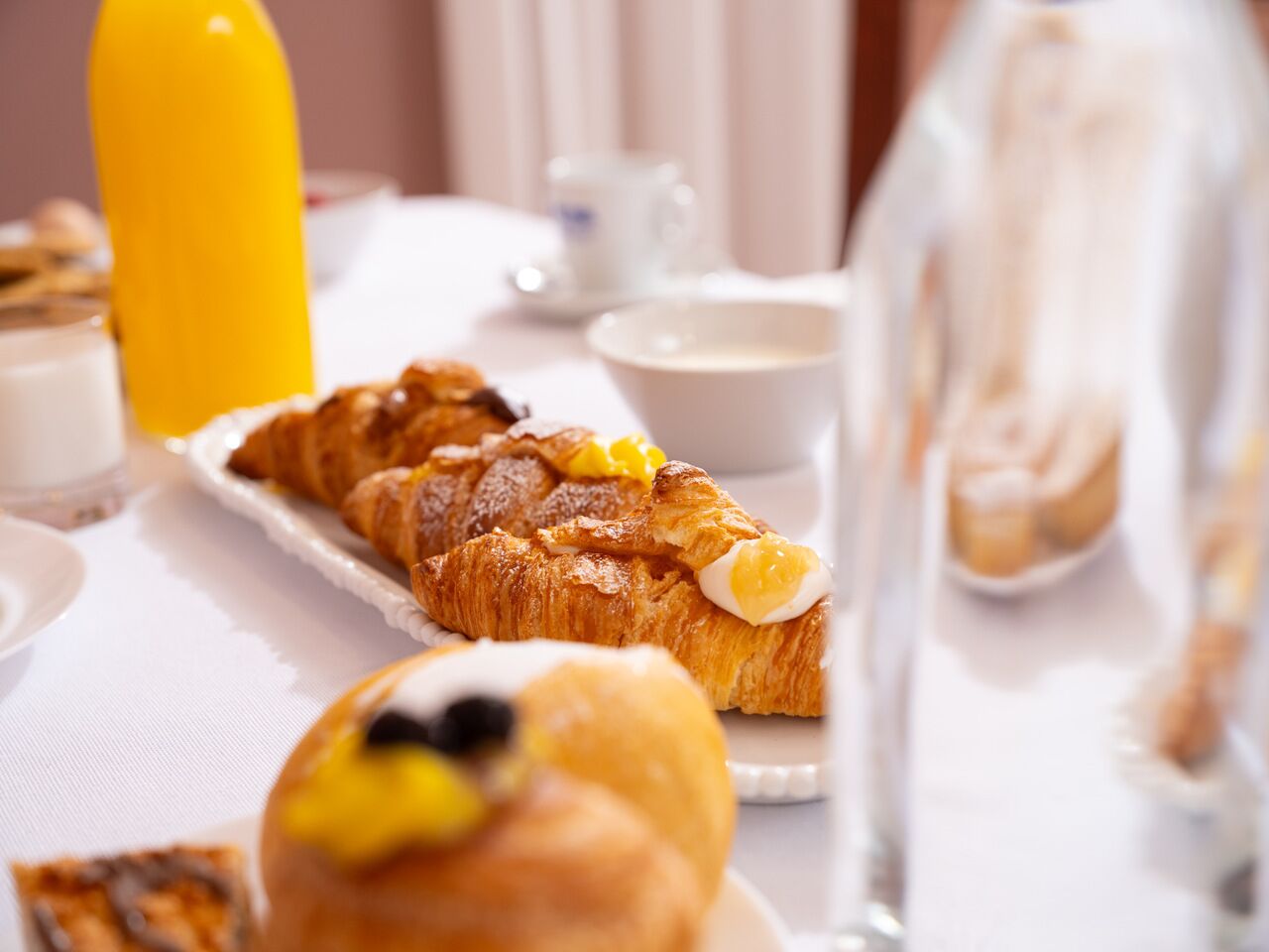 Mesa com croissants, garrafa de sumo de laranja e copo de leite.