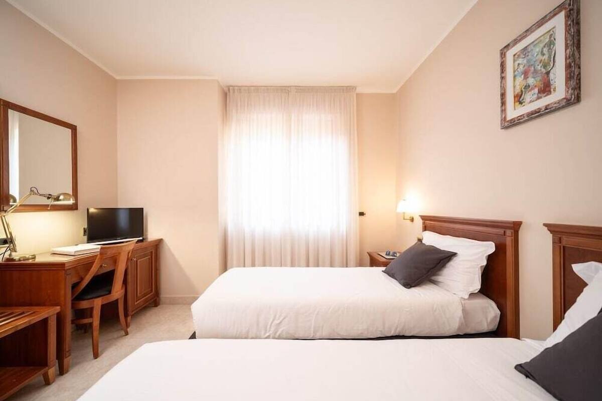 Ein Hotelzimmer mit einem Bett, einem Schreibtisch, einem Sessel, einem Fernseher und einem Bild an der Wand.