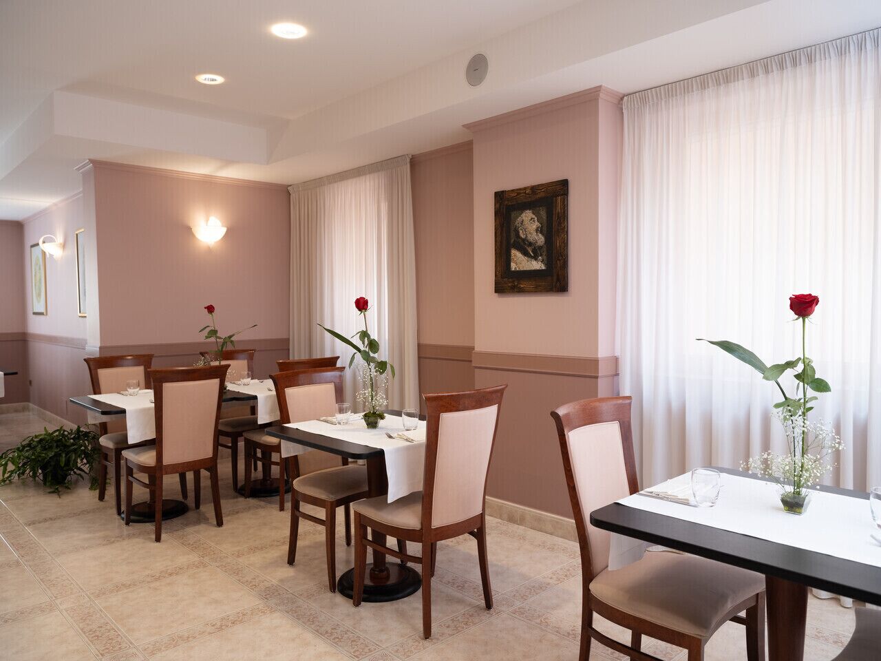 A dining area with tables set for four, each with a vase of flowers and a candle.