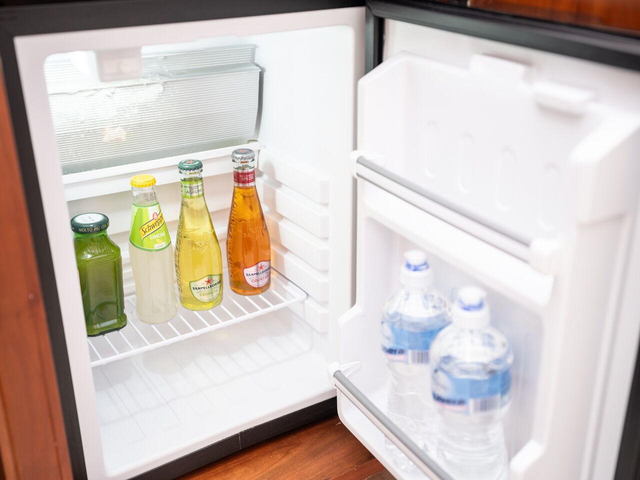 Un refrigerador abierto con estantes que contienen botellas de bebidas y agua.