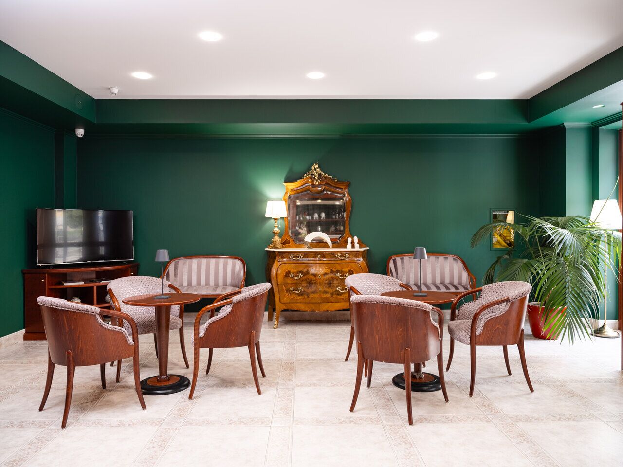 A room with a green wall, a wooden cabinet, a television, and a dining area with chairs and a table.