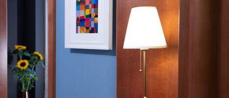 A hallway with a framed abstract painting, a round table with a lamp, and a vase with sunflowers.