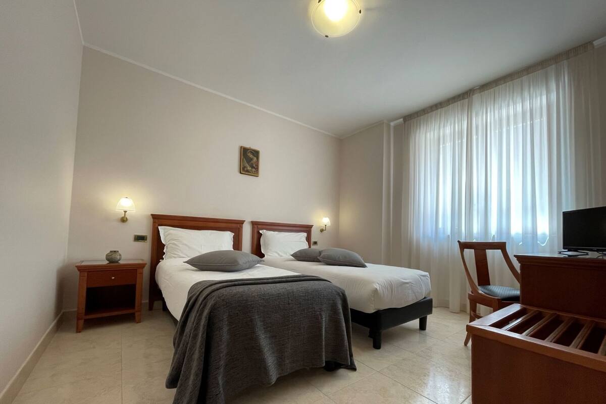 Ein Hotelzimmer mit zwei Betten, einem Schreibtisch, einem Stuhl, einem Fernseher und einer Lampe.