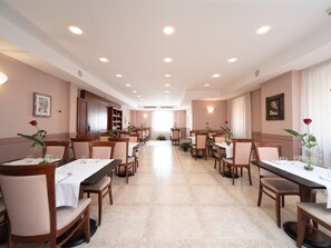 A spacious dining area with multiple tables and chairs, a central aisle, and ceiling lights. - Hotel San Pio (San Giovanni Rotondo)