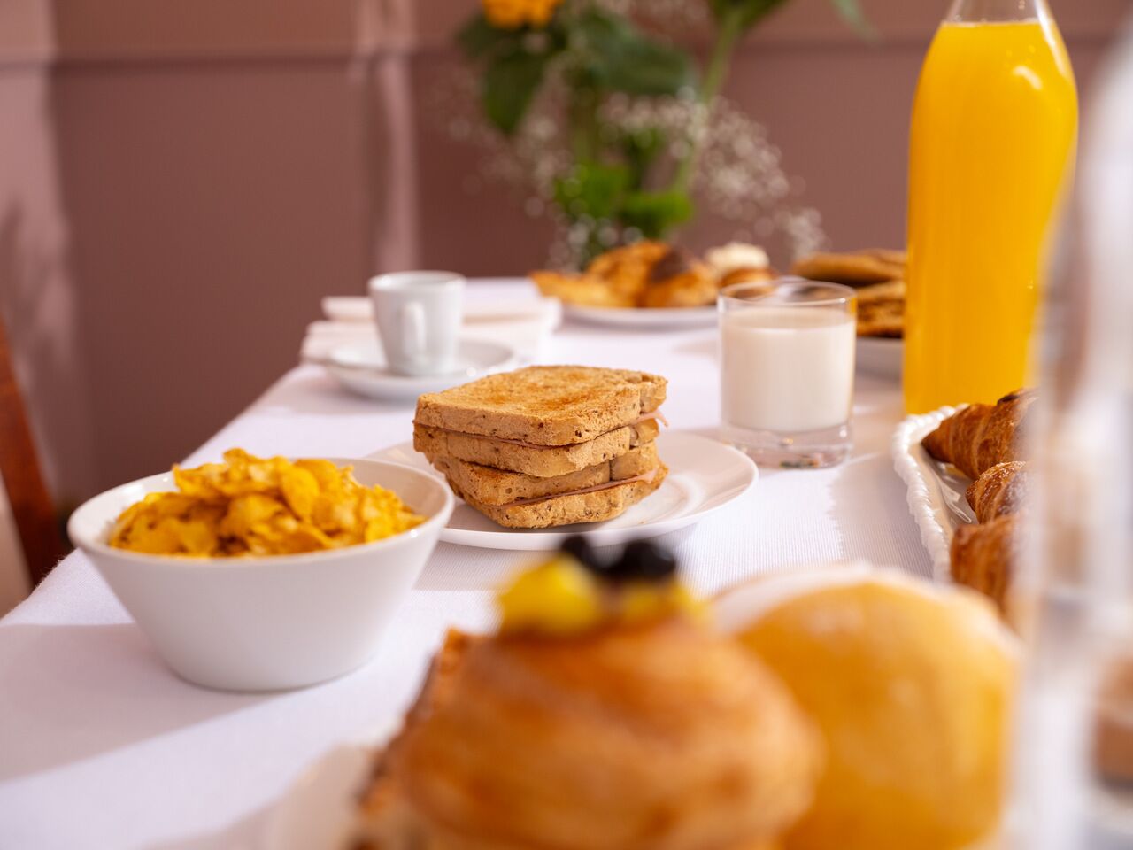 A breakfast table with toast, a bowl of fruit, a glass of milk, and croissants.