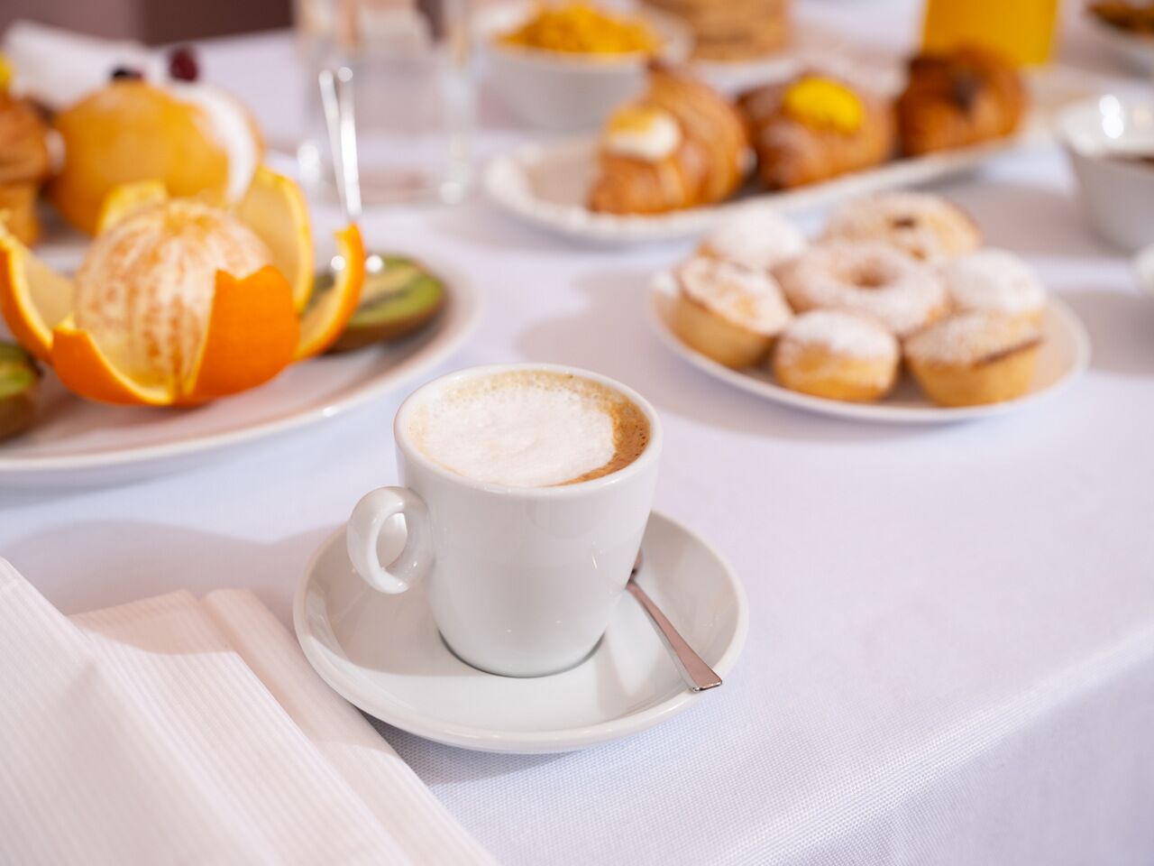 A breakfast setting with a cup of coffee, pastries, and fruit on a table.