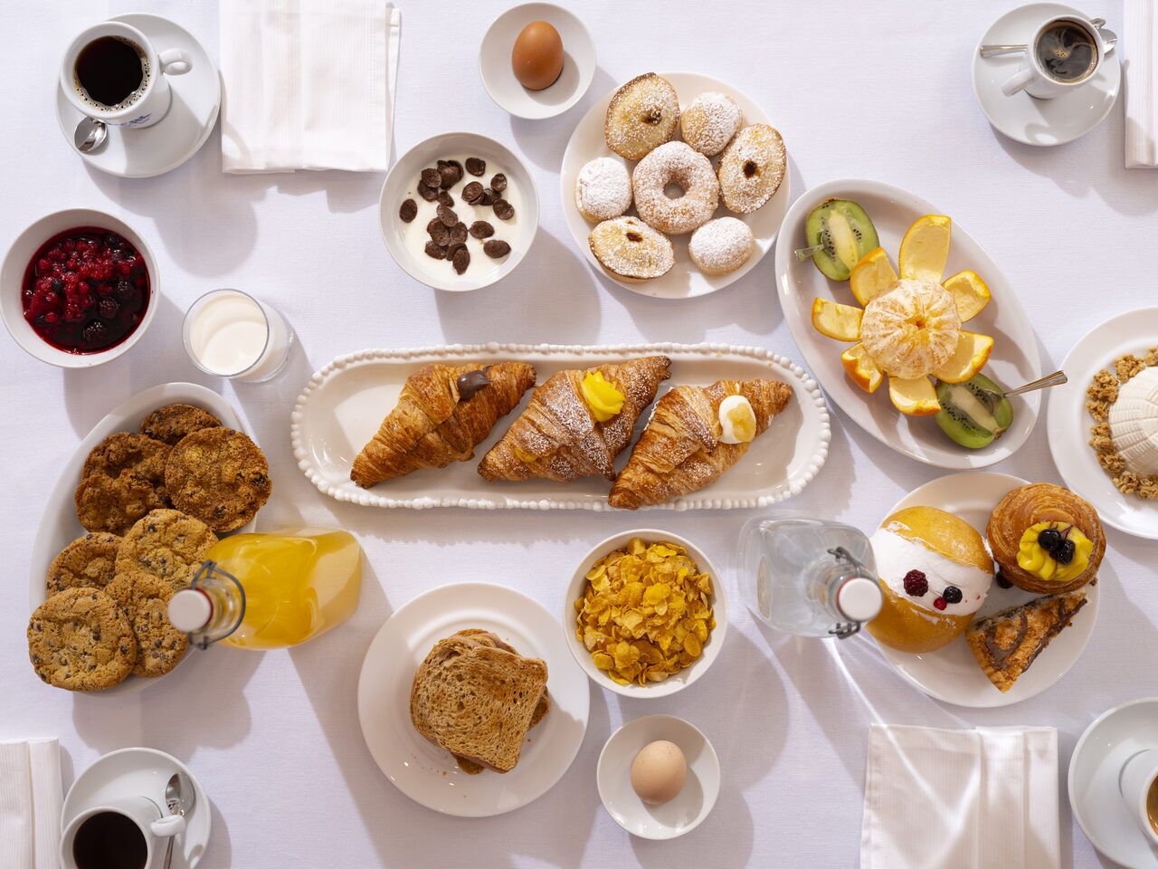 Una mesa blanca con una bandeja de desayuno que incluye varios pasteles, frutas y bebidas.