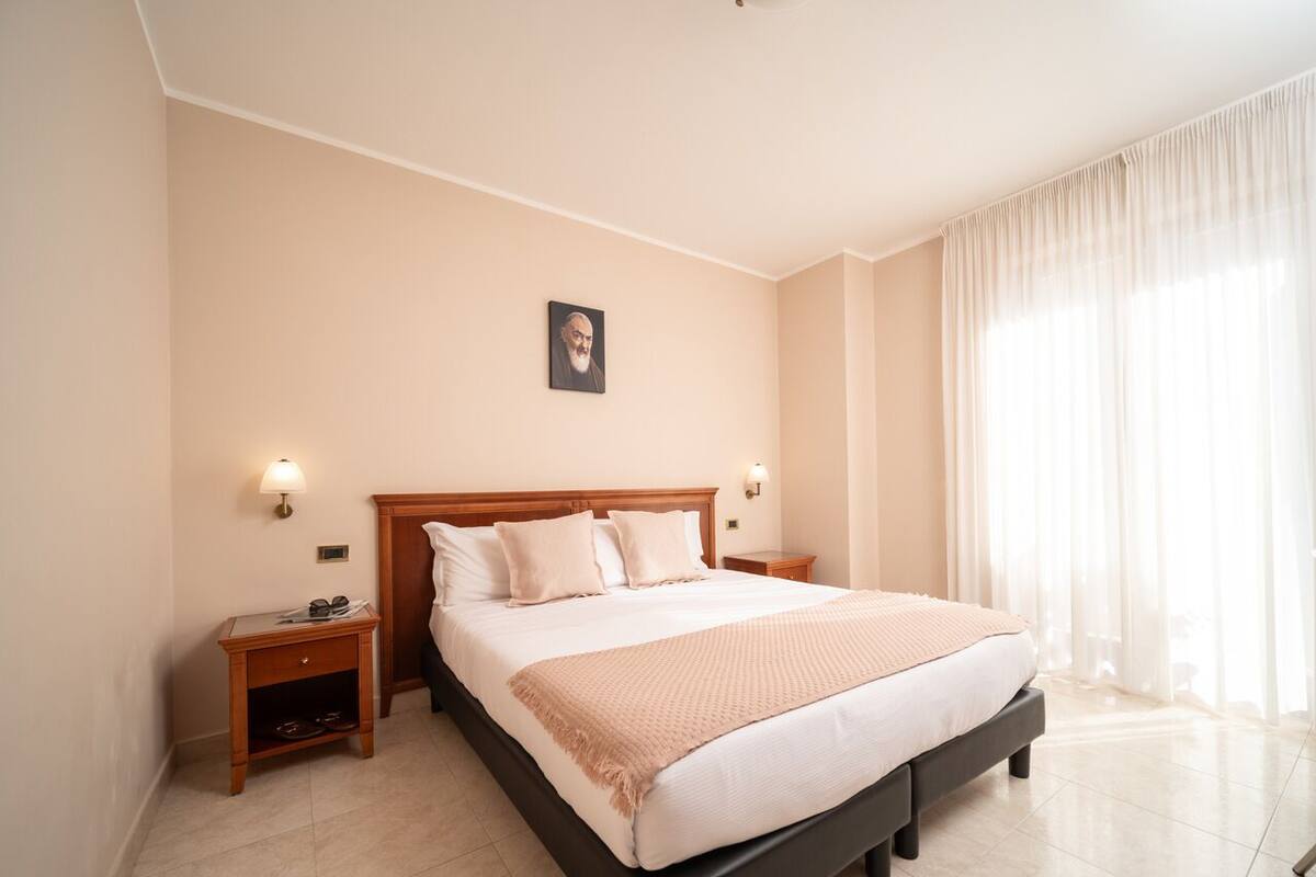Ein Hotelzimmer mit einem großen Bett, Nachttischen, einer Kopfteil und einem Fenster mit Vorhängen.