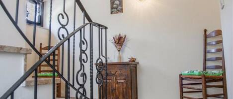 A staircase with ornate metal railings, a wooden cabinet, a chair, and a wall-mounted light fixture.