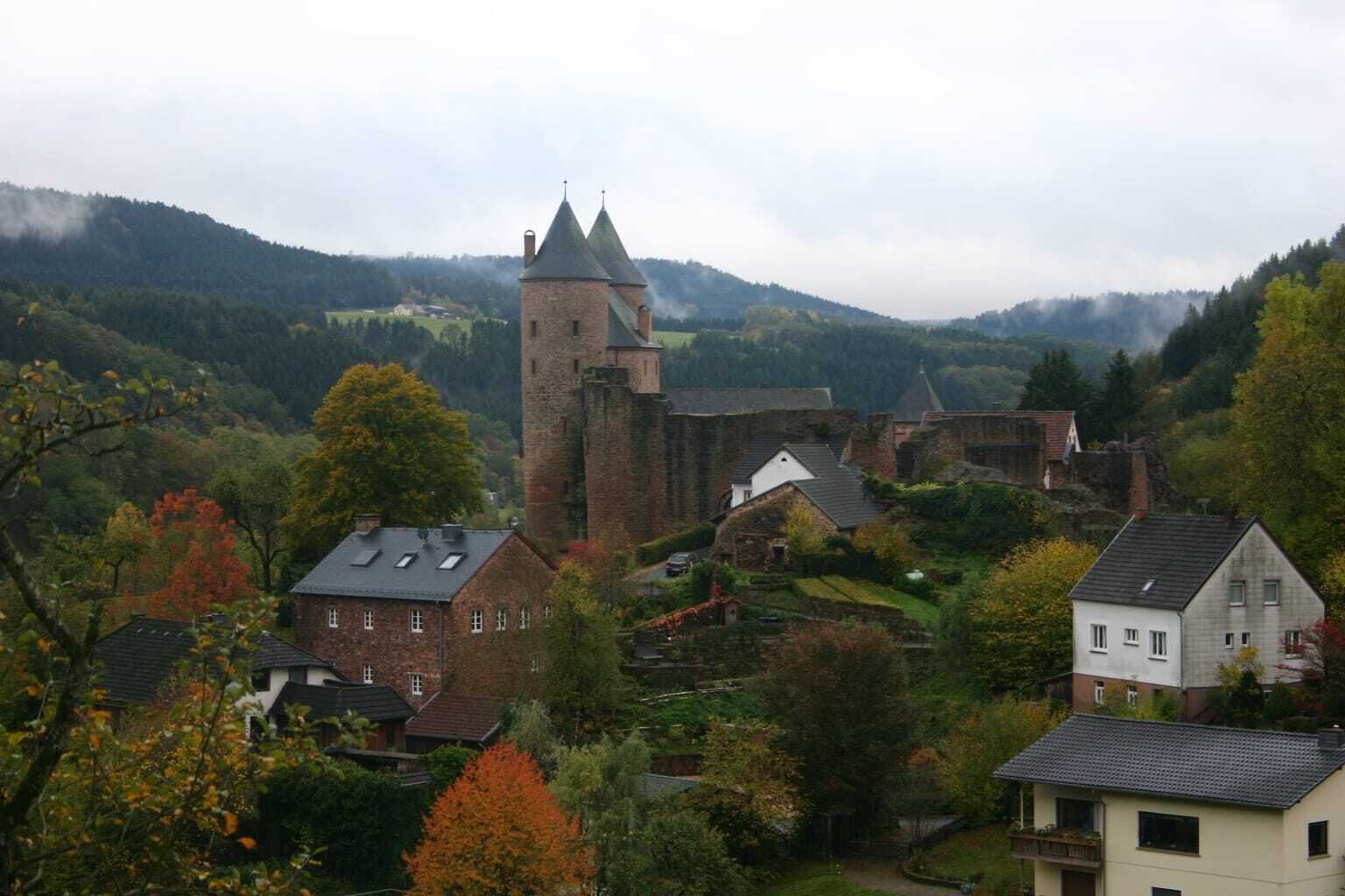 Una città storica con una torre imponente, circondata da edifici residenziali e rigogliosa vegetazione.
