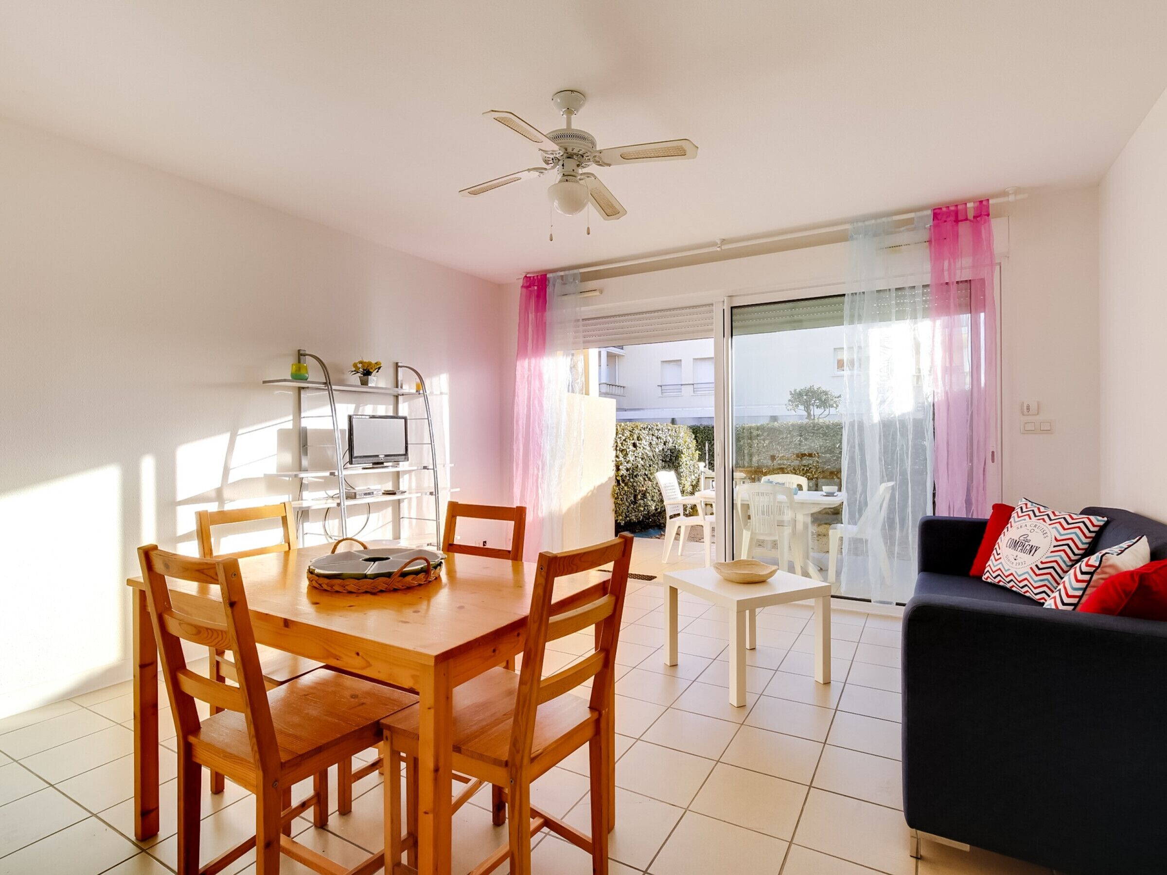 A dining area with a wooden table and chairs, a ceiling fan, and a view of the outdoors through a glass door.