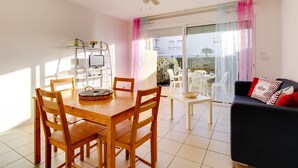 A dining area with a wooden table and chairs, a ceiling fan, and a view of the outdoors through a glass door. - Biscarrosse: Appartement T3, 2 Chambres, Terrasse, Parking Privé à 50m de la Plage (Biscarrosse Plage)