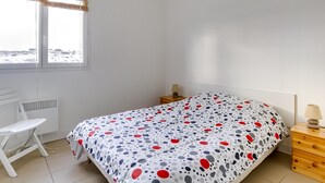 A bedroom with a bed, a desk, a chair, a bedside table, and a window with curtains. - Biscarrosse: Appartement T3, 2 Chambres, Terrasse, Parking Privé à 50m de la Plage (Biscarrosse Plage)