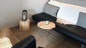 A modern living room with a black sofa, a round mirror, a small round table, and a woven pouf. - Le Bastidon de l'Olivier (Gordes)