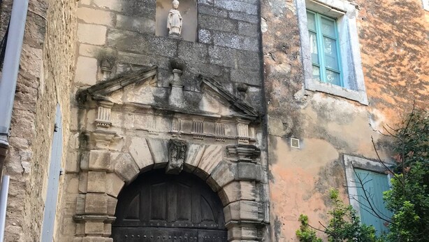 A stone building with a large arched entrance, a statue above the door, and a window with blue shutters. - Le Bastidon de l'Olivier (Gordes)