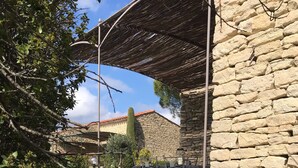 A stone building with a covered outdoor seating area. - Le Bastidon de l'Olivier (Gordes)