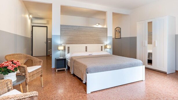 Un dormitorio moderno con una cama grande, lámparas de noche, un sillón de mimbre y un armario.