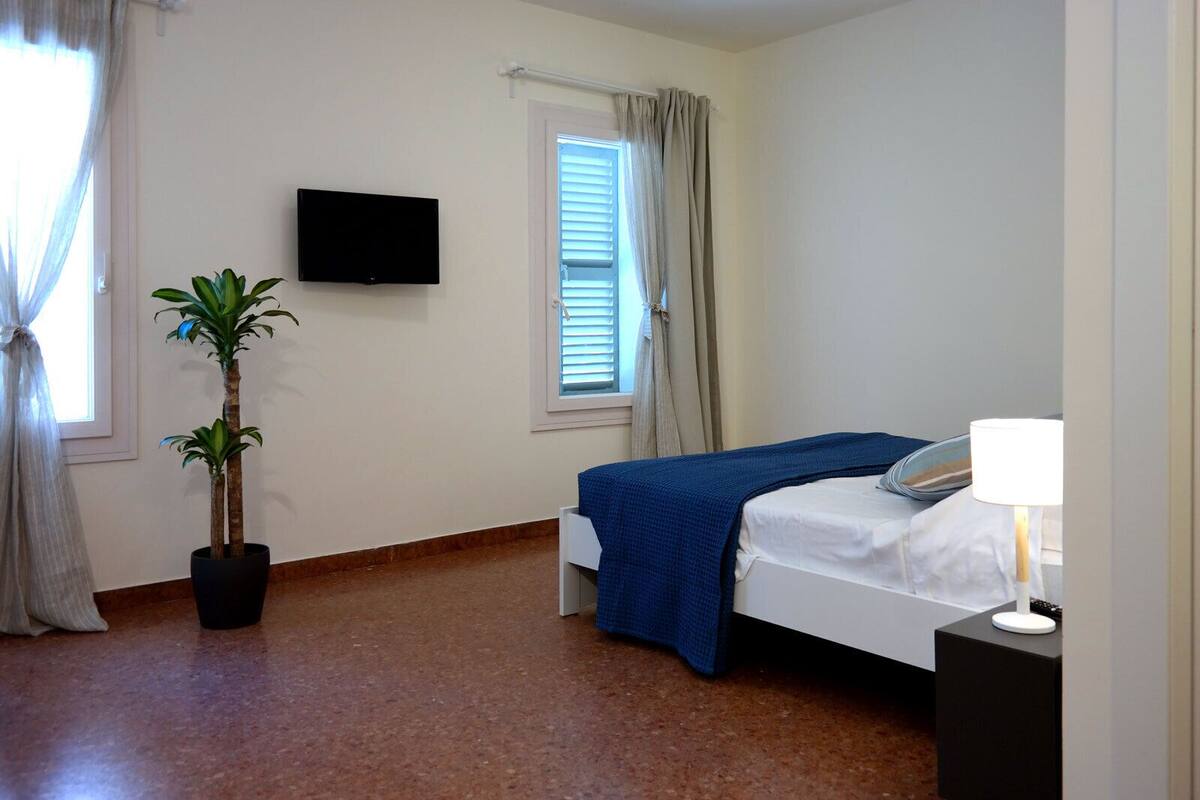 A bedroom with a bed, a TV mounted on the wall, a potted plant, and a bedside lamp.