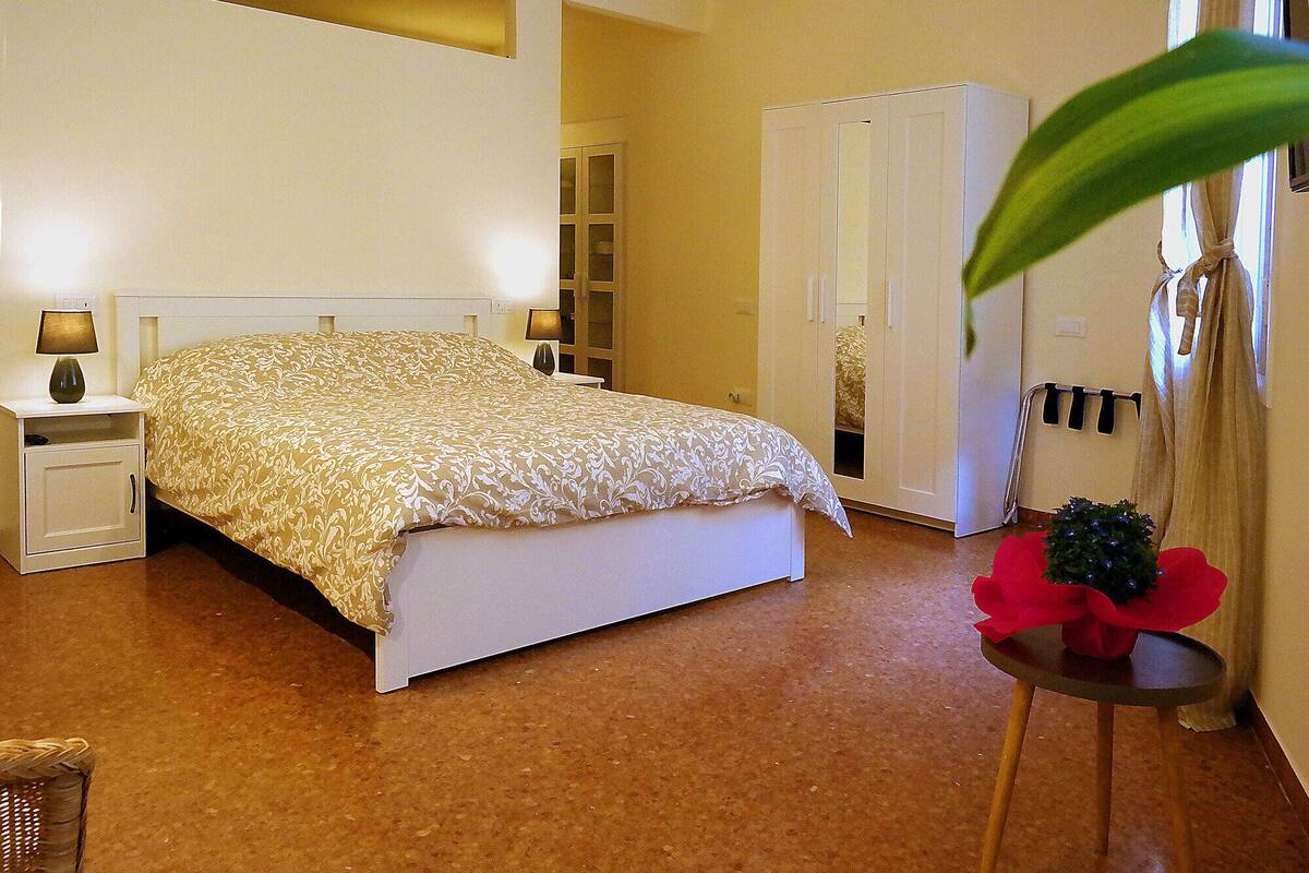 A bedroom with a bed, nightstands, a wardrobe, and a small table with a plant.