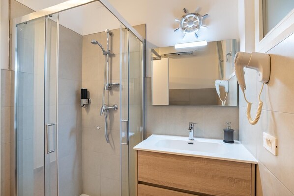 A modern bathroom with a glass shower enclosure, a white sink with a wooden vanity, a hairdryer, and a mirror with a ship wheel light. - Marinali Rooms (Bassano del Grappa)