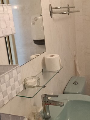 A bathroom with a glass shelf holding a glass bowl, a toilet paper holder, and a mirror. - La Meridienne (Sète)