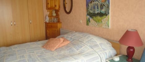 A bedroom with a bed, a nightstand, a lamp, a dresser, a mirror, and a painting on the wall.