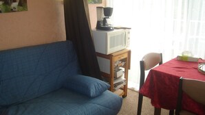Una sala de estar con un sofá azul, una mesita de madera con un microondas y una mesa cubierta con mantel rojo.
