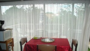 Un comedor con una mesa cubierta por un mantel rojo, sillas, una mesita con una bandeja y un televisor sobre un mueble.
