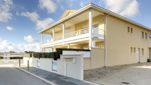 Un immeuble de deux étages doté d’un balcon à l’étage supérieur, d’une entrée fermée par un portail et d’une allée gravillonnée.