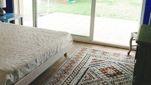 Un dormitorio con cama, un tapete estampado y vistas a una pequeña casita de juegos a través de una puerta corrediza de vidrio.