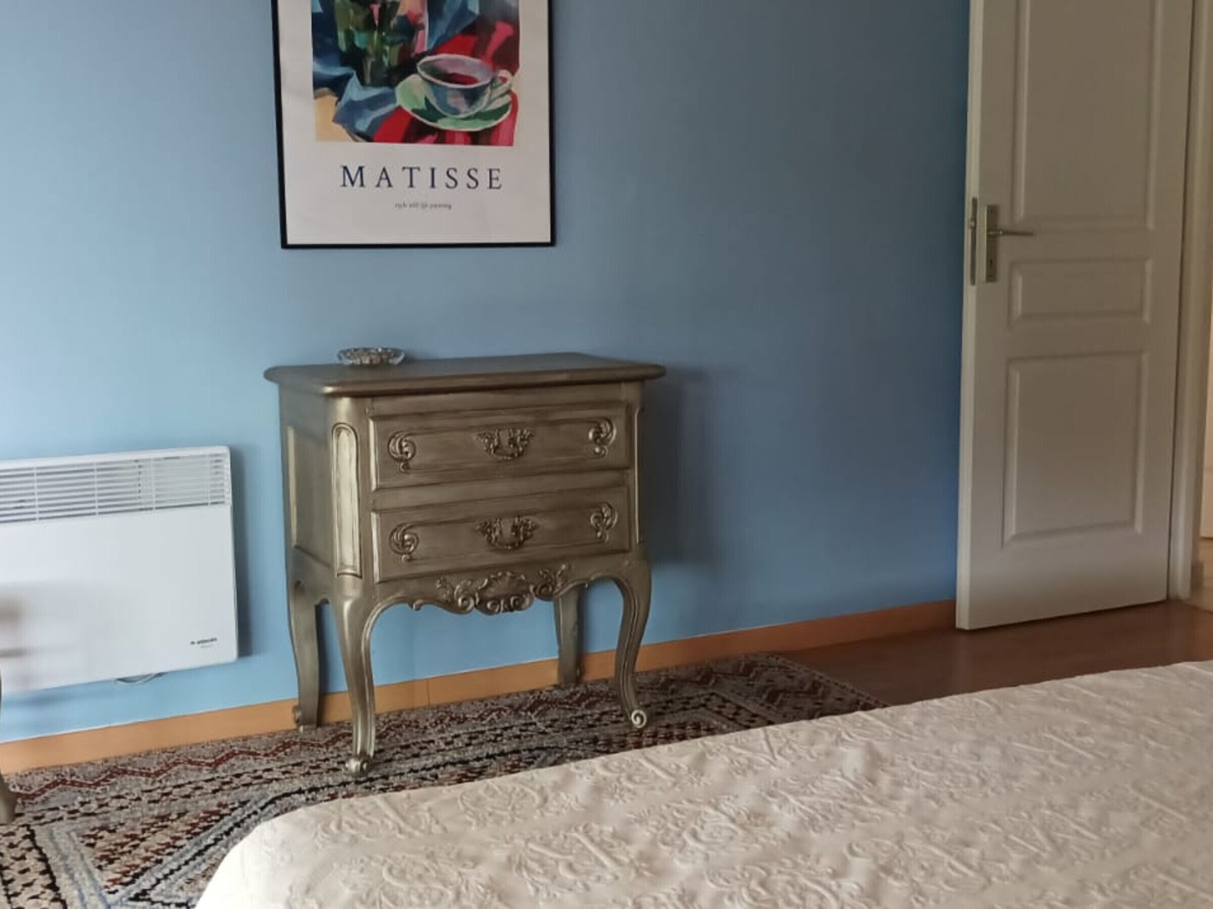 Una camera da letto con un letto, una cassettiera, un termosifone e una porta.