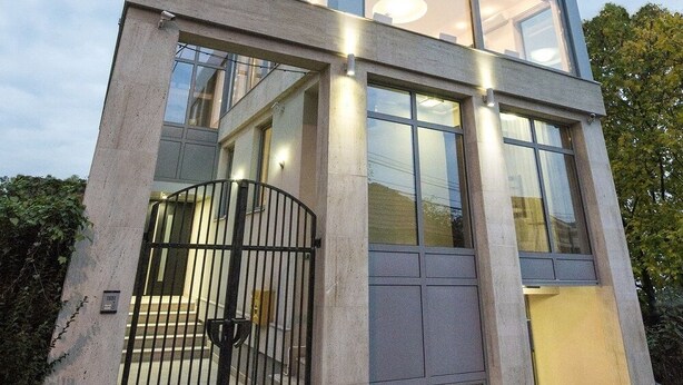 Un edificio moderno con fachada de vidrio, un logotipo central y una puerta metálica.