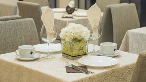 Una mesa de comedor dispuesta con platos blancos, tazas y un florero de vidrio con flores blancas.