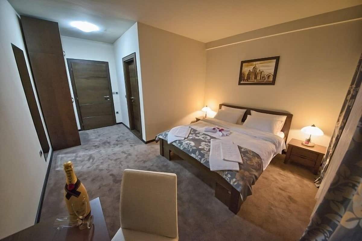 Quarto de hotel com cama, abajures, uma cadeira, escrivaninha e uma porta.