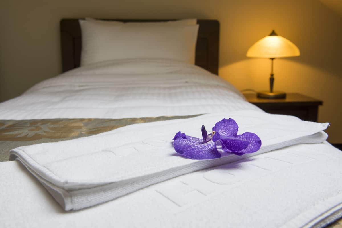 Uma cama bem arrumada com edredom branco e uma flor roxa no travesseiro.
