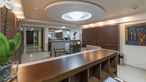 Un moderno vestíbulo de hotel con un mostrador de recepción central, una zona de bar y un espacio para comer.