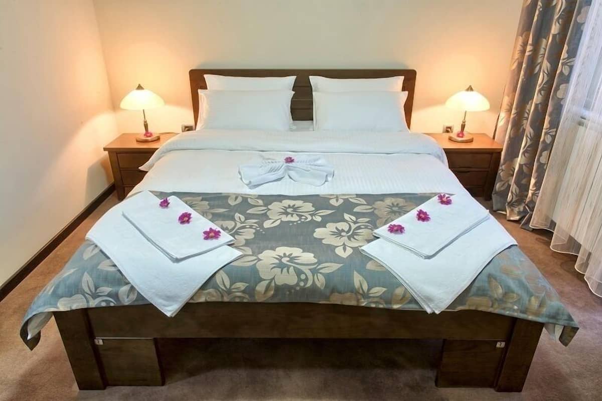 Uma cama bem arrumada com colcha florida, duas luminárias de cabeceira e cortina florida.