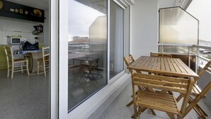 Un balcon avec une table et des chaises en bois, une porte-fenêtre coulissante et un coin cuisine équipé d’un four à micro-ondes et d’une machine à café.