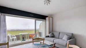 Une pièce avec un balcon, un canapé gris, une chaise en bois et une table.