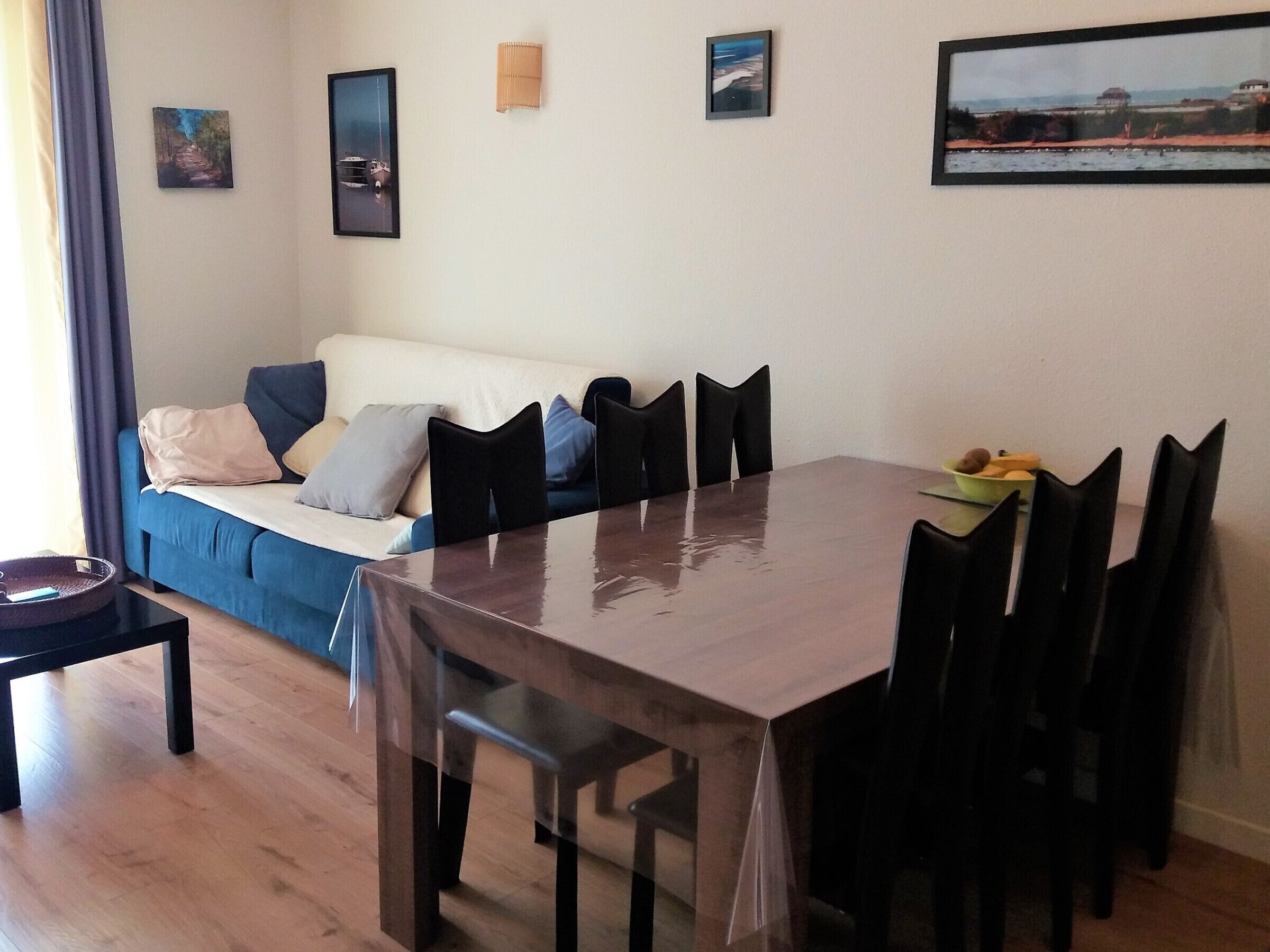 Un comedor con una mesa y sillas de madera, un sofá azul con cojines, y una mesita con un tazón.