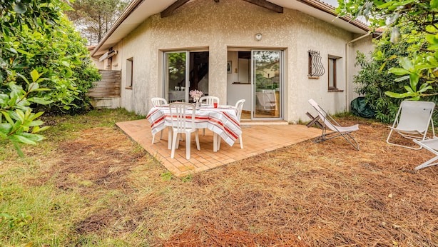 A house with a patio, a dining table with chairs, and a sliding glass door. - Charming 4-Person Home, Quiet Area Near Beaches, Biscarrosse (Biscarrosse Plage)
